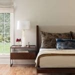 Dark wood bed frame with patterned throw pillows and a side table.
