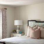 Cream-colored bedroom with a bed, lamp, and curtains.