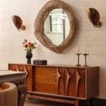 Wooden dresser with brass wall sconces and a rattan mirror.