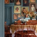 Dark teal wall with vintage portraits, wooden table, and chairs.