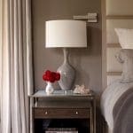 Gray bedside lamp on a wooden nightstand with books and flowers.