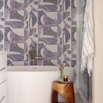 Purple geometric wallpaper, bathtub, wooden side table with candles.