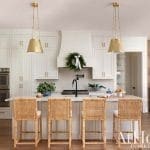 White kitchen with brass pendant lights and a wood island.