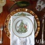 Gold charger plate, floral plate, silverware, and napkins on a wooden table.