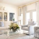 White living room with blue and white cabinets, curtains, and a glass coffee table.
