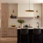 Light wood kitchen island with black bar stools and marble backsplash.