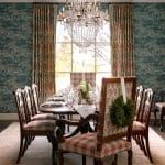 Dining room with a large crystal chandelier, patterned wallpaper, and wooden chairs.