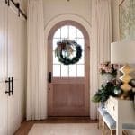 Arched entryway with white drapes, wreath, and wooden door.