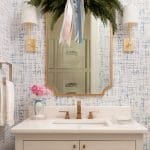 Powder room with blue and gray patterned wallpaper, mirror, and gold fixtures.