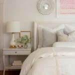 White bed with gray pillows, a mirror, and a lamp.