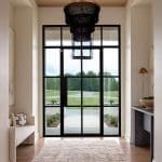 Black metal entry door with a woven light fixture and wood paneling.