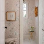 Pink wallpaper with bird motif, gold light fixture, and patterned chair.