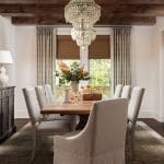 Dining room with beaded chandelier, wooden table, and neutral drapery.