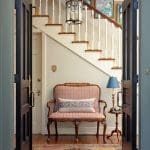Blue entryway with a wooden staircase, patterned rug, and seating.
