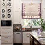 White kitchen cabinets with gold hardware, roman shade, and marble countertop.