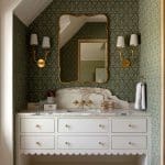White vanity with marble countertop and gold fixtures in a green-patterned room.
