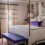 Four-poster bed with patterned wallpaper, curtains, and purple bench.