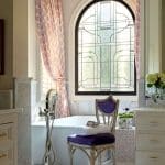 Marble bathroom with arched stained-glass window and purple chair.