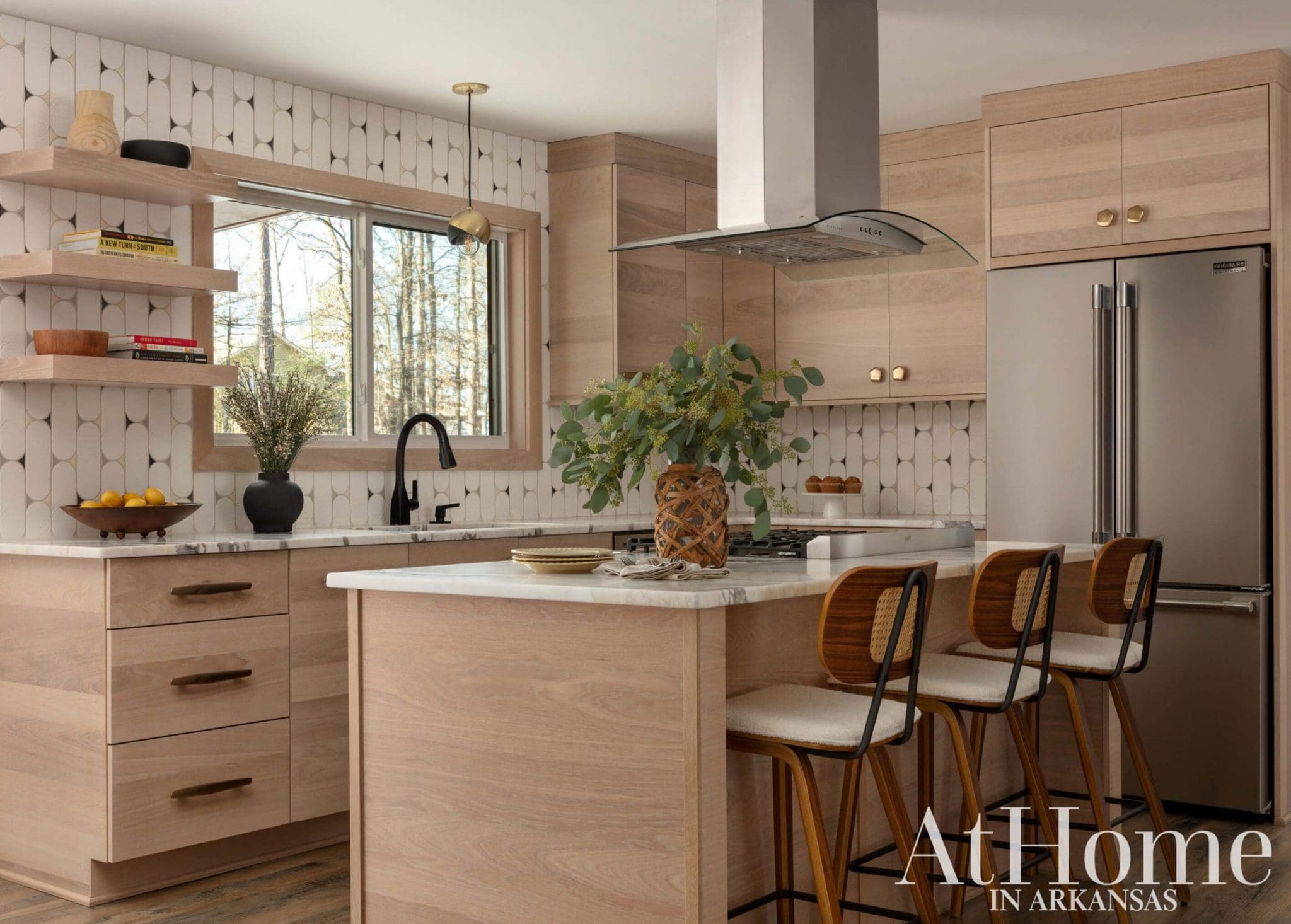 Light wood kitchen with marble island, geometric backsplash, and stainless steel appliances.