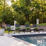 Poolside lounge chairs with green pillows next to a swimming pool.