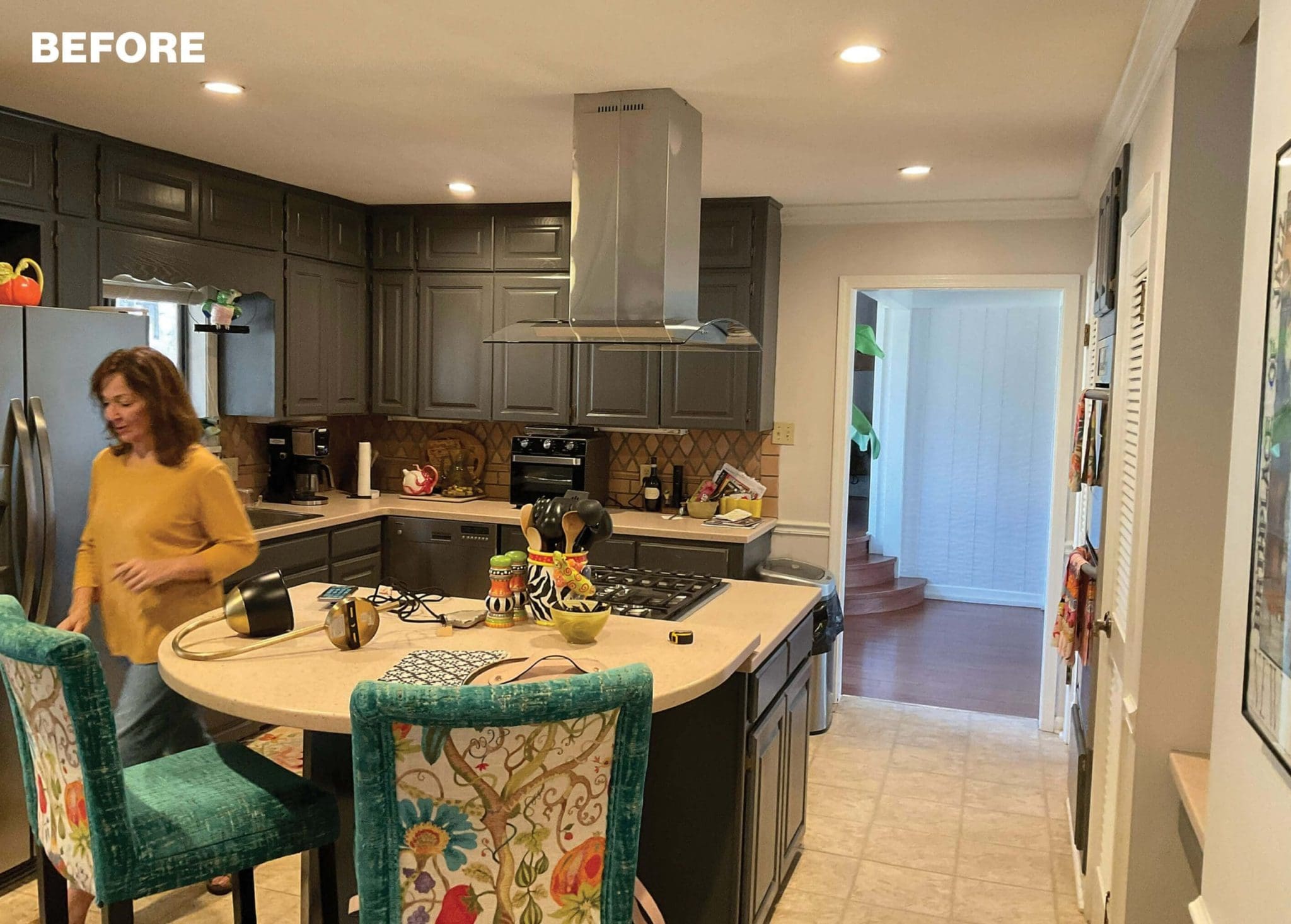 Dark gray kitchen cabinets, stainless steel range hood, and island with patterned chairs.