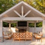 Covered patio with stone fireplace, outdoor seating, and white brick walls.