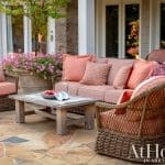 Wicker patio furniture with coral cushions on flagstone patio, pink flowers in pots.