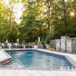 Swimming pool with stone waterfall feature and lounge chairs, surrounded by trees.