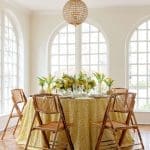 Dining room with yellow floral tablecloth, bamboo chairs, and crystal chandelier.