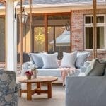 Covered porch with swing sofa, patterned armchair, wooden coffee table, and brick wall.