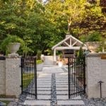 Brick wall with black wrought iron gate, stone pathway, and landscaping.