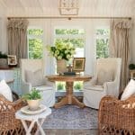 Sunroom with white wingback chairs, wicker chairs, round wood table, and floral arrangement.