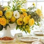 Yellow and white floral arrangement with lemons on a table set with patterned plates.