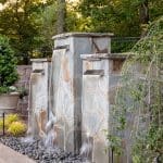 Stone waterfall feature with multiple tiers, surrounded by trees and landscaping.