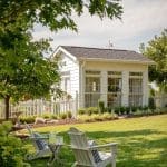White sunroom with large windows, white picket fence, and Adirondack chairs on lawn