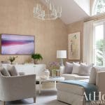 Tan wallpapered room with a chandelier, sofa, and artwork.