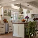 White kitchen with wooden beams, island, and green chairs.