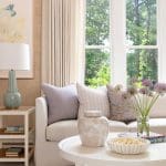 Cream sofa with light gray pillows, window view, and floral arrangement.