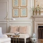 Wall arrangement of botanical prints, a sofa, and a marble fireplace.