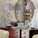 Purple wallpaper with floral and bird motifs, a mirror, and table lamps.