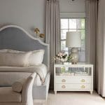 Gray upholstered headboard with bedside table and window view.