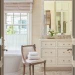 White bathroom with marble vanity, window, and chair.