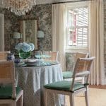 Dining room with patterned wallpaper, chandelier, and wicker chairs.
