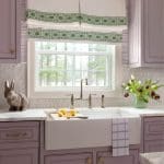 Purple kitchen cabinetry with patterned window treatment and floral arrangement.