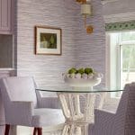 Blue and white striped wallpaper, gold chandelier, wicker chairs, and fruit bowl.