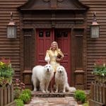 Brown shingle house with red door and flanking dogs.