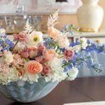 Large gray vase filled with pink and blue flowers on a dark wood table.