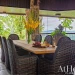 Outdoor dining table with rattan chairs, flowers, and a view.