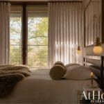 Bedroom with sheer curtains, a bed, and a window overlooking trees.