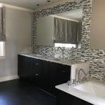 Gray tiled wall with mirror and window, black vanity, and white countertop.